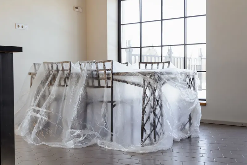 Table and chairs covered in clear plastic sheeting in a bright room