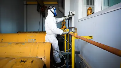 Worker in a white protective suit and respirator at industrial equipment